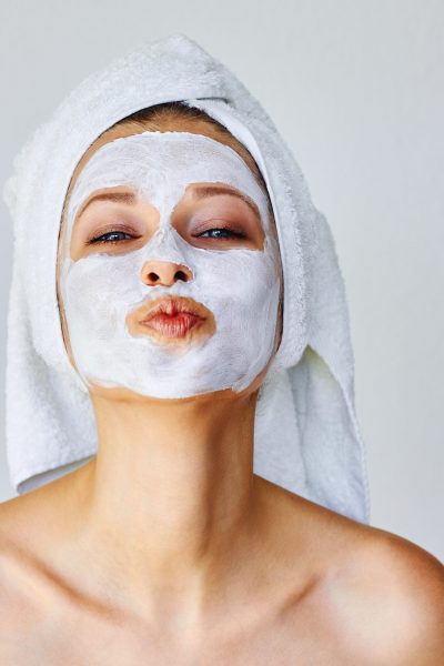 Beautiful young woman with facial mask on her face. Skin care and treatment, spa, natural beauty and cosmetology concept