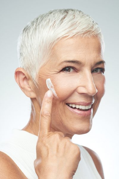 Gorgeous smiling Caucasian senior woman trying out new anti age cream. Beauty photography.